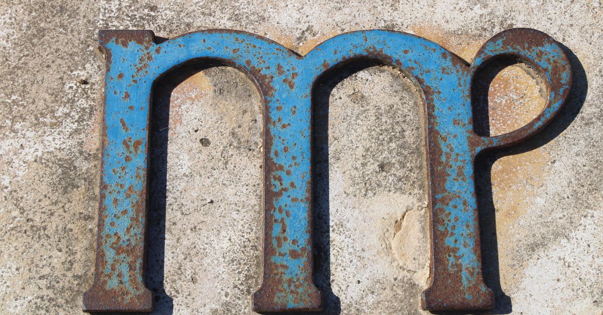 Close-up of a rusty, blue metal letter on a textured concrete background, showcasing decay and texture.